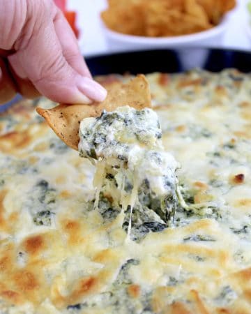 Spinach Artichoke Dip being scooped with tortilla chip