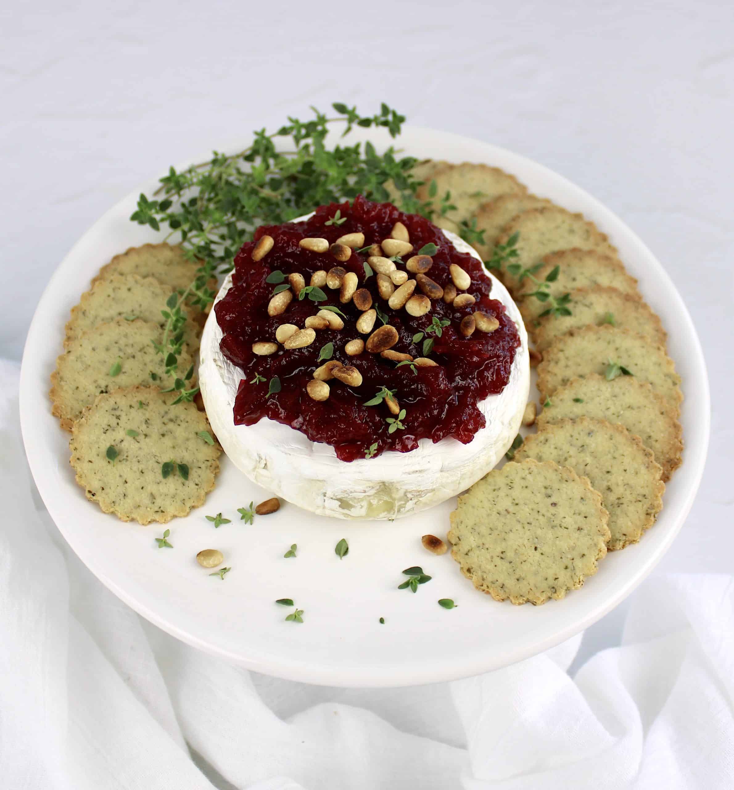 baked brie with cranberry sauce and pine nuts on top with crackers on the side