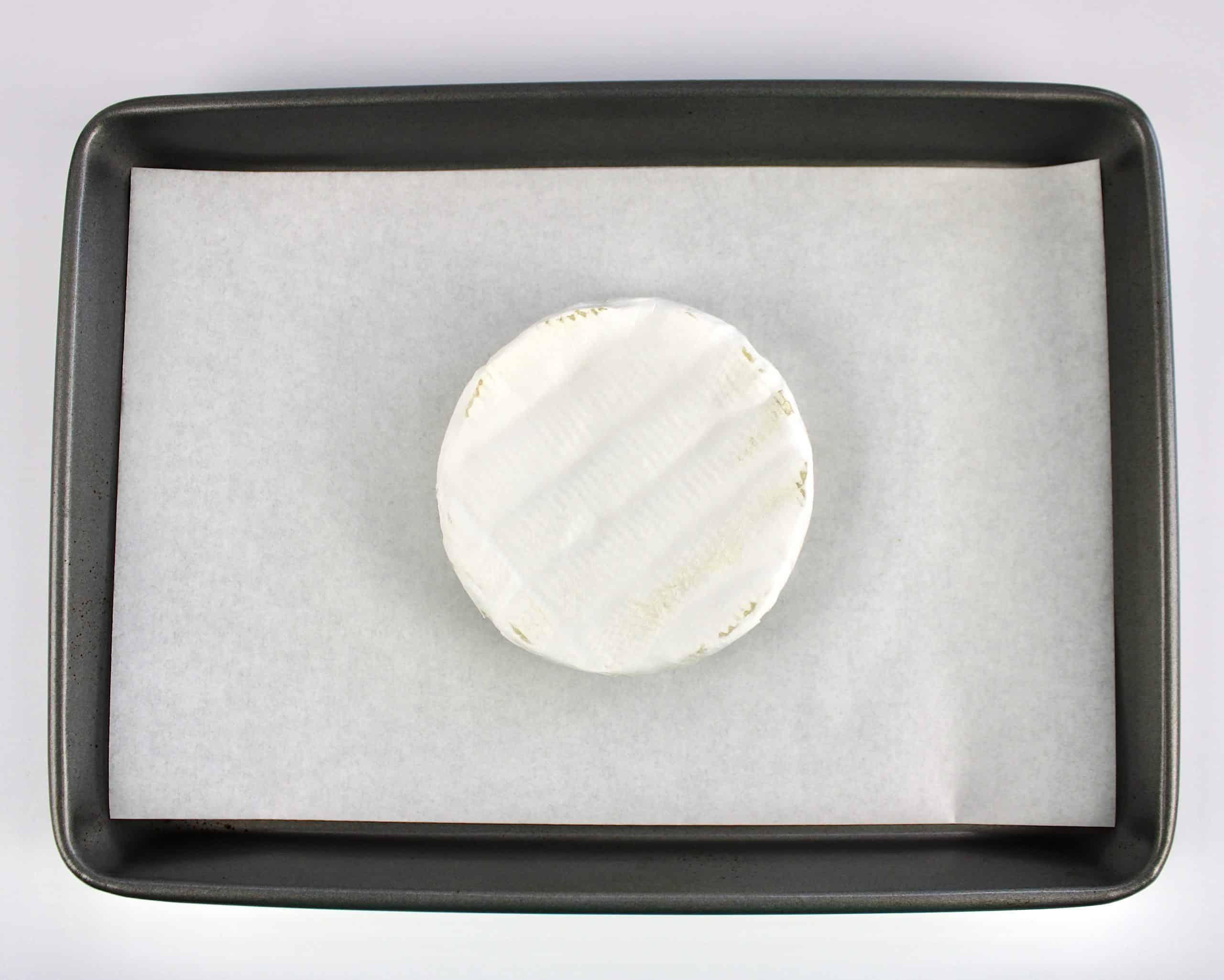 unbaked wheel of brie cheese on white parchment paper on baking sheet