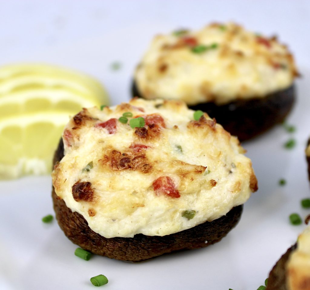 closeup of Crab Stuffed Mushroom on white plate with another in background and lemon slices