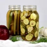 closeup of 2 jars of pickles slices and spears with onion and dill on side