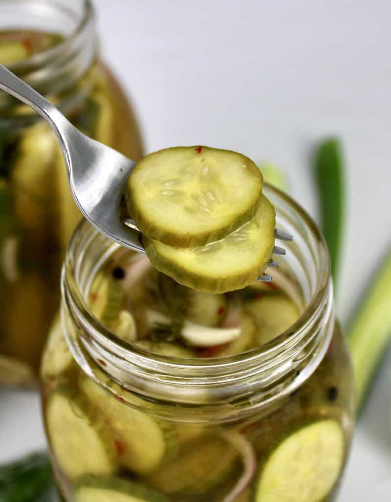 jar of homemade pickle slices with fork holding up two