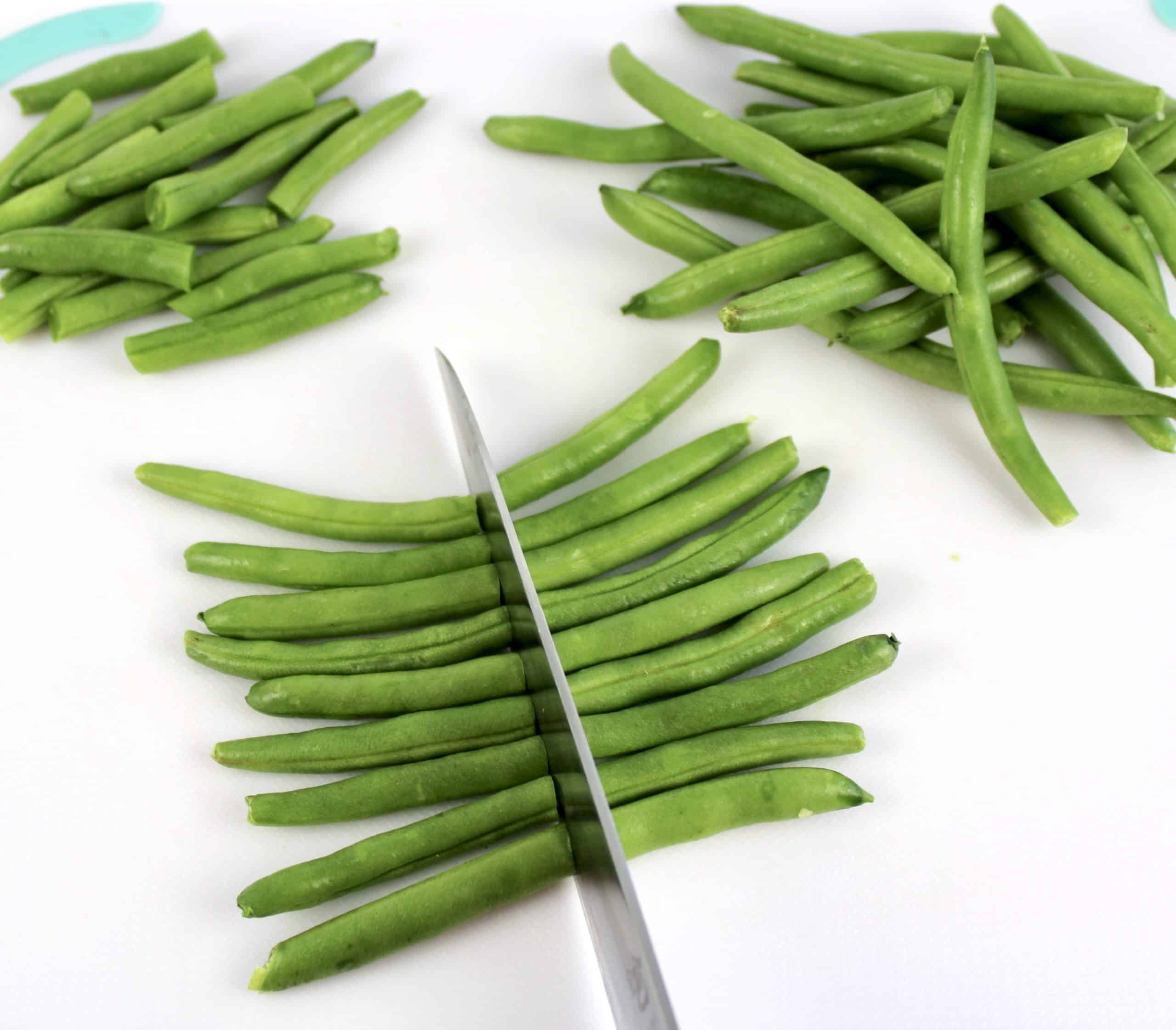 green beans on white cutting board being cut in half
