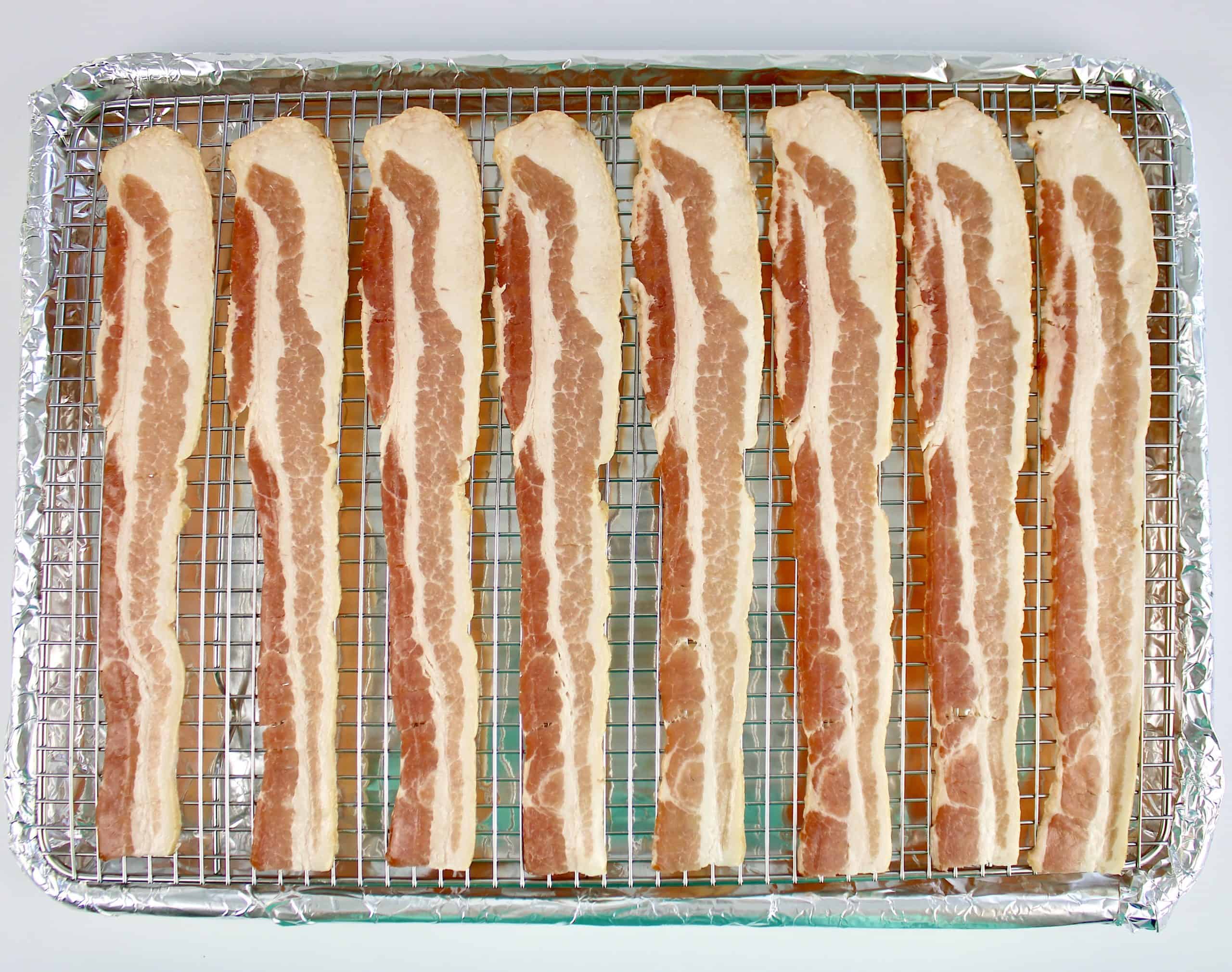 raw strips of bacon on wire rack and baking sheet