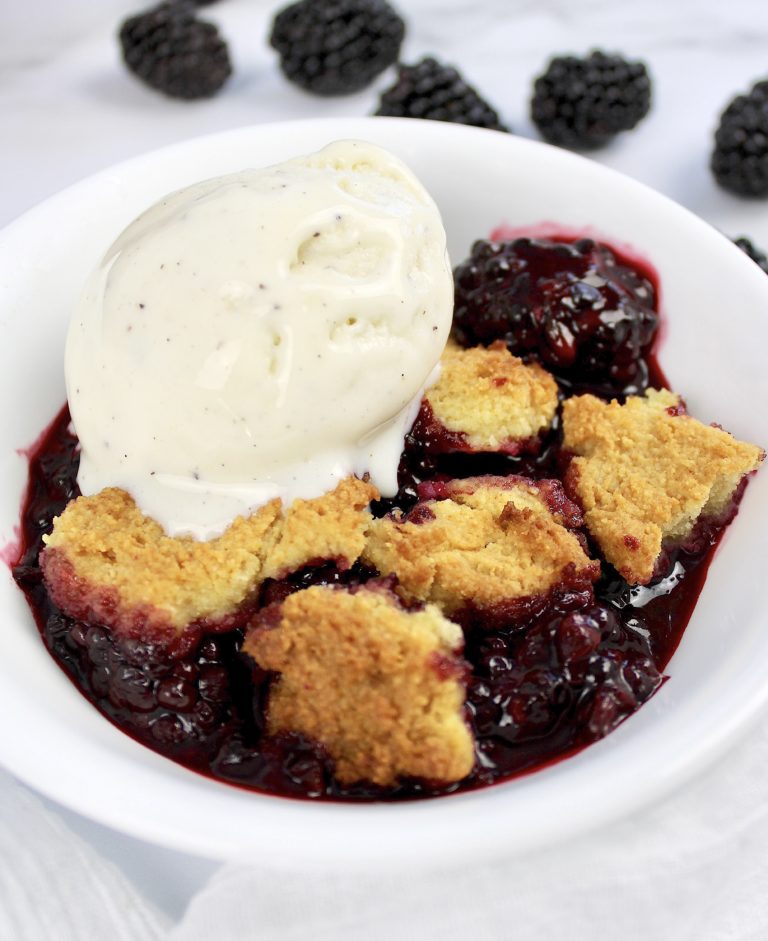 blackberry cobbler in white dish with scoop of vanilla ice cream on top