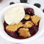 blackberry cobbler in white dish with scoop of vanilla ice cream on top