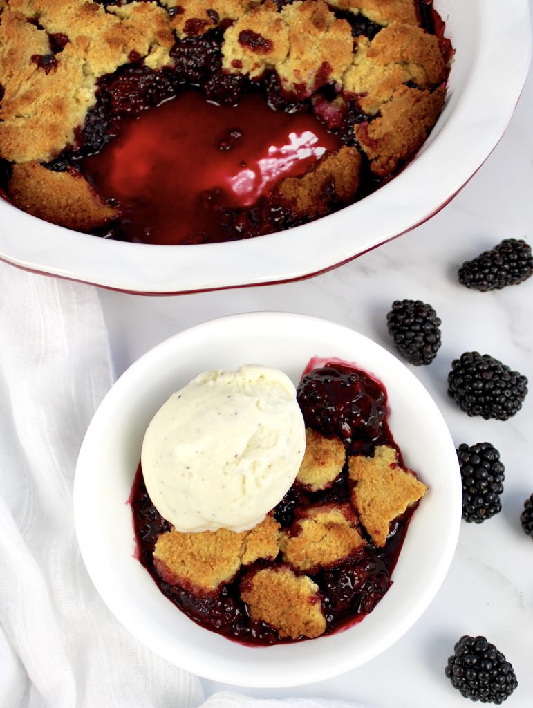 blackberry cobbler with ice cream on top with pie in background