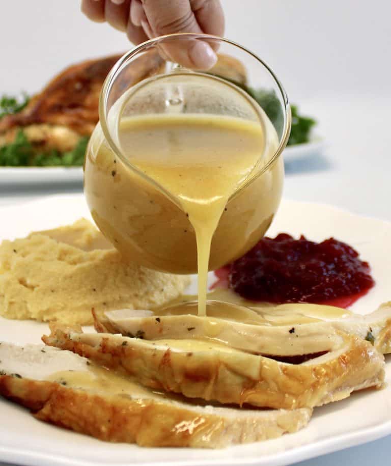 gravy being poured over sliced turkey on white plate