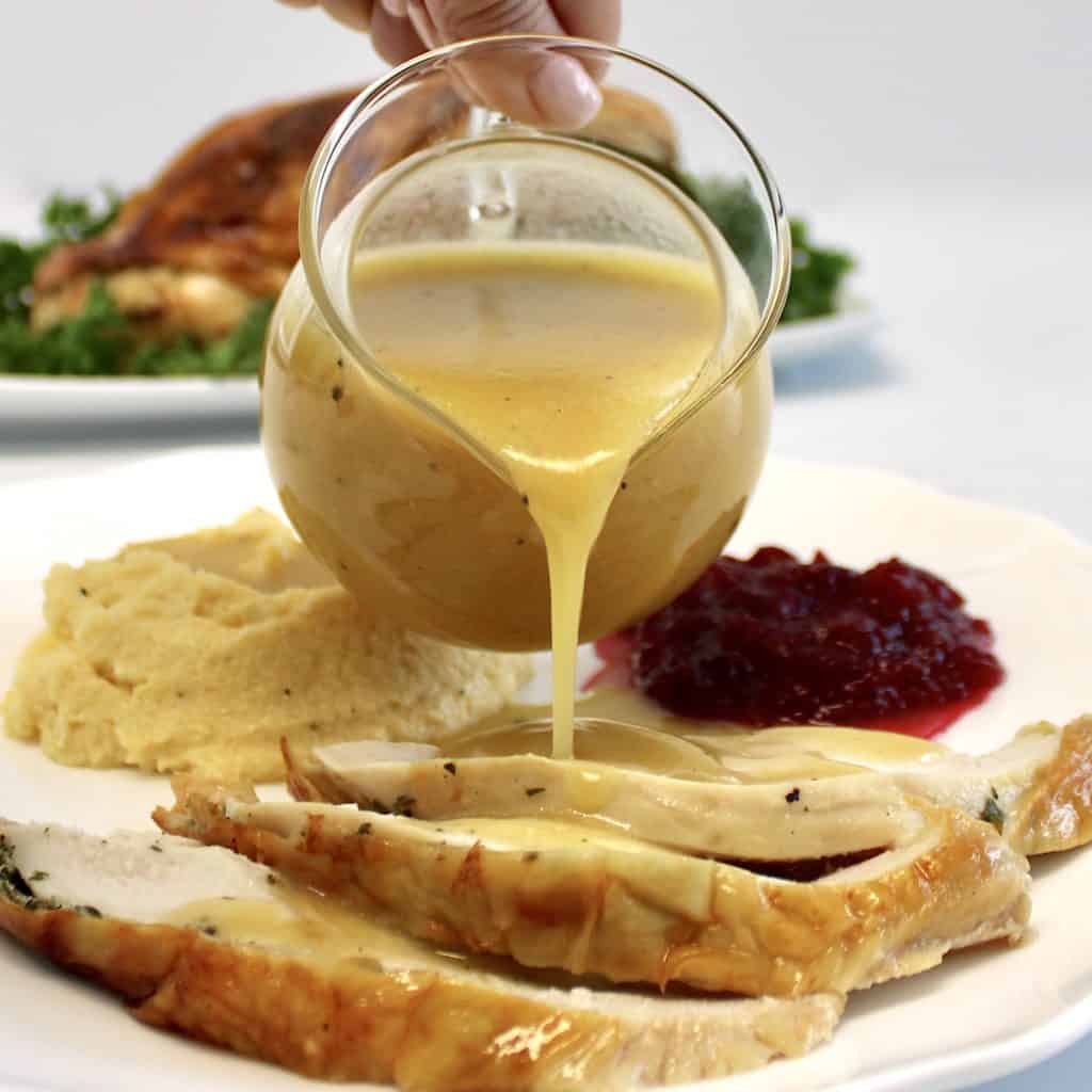 gravy being poured over sliced turkey on white plate