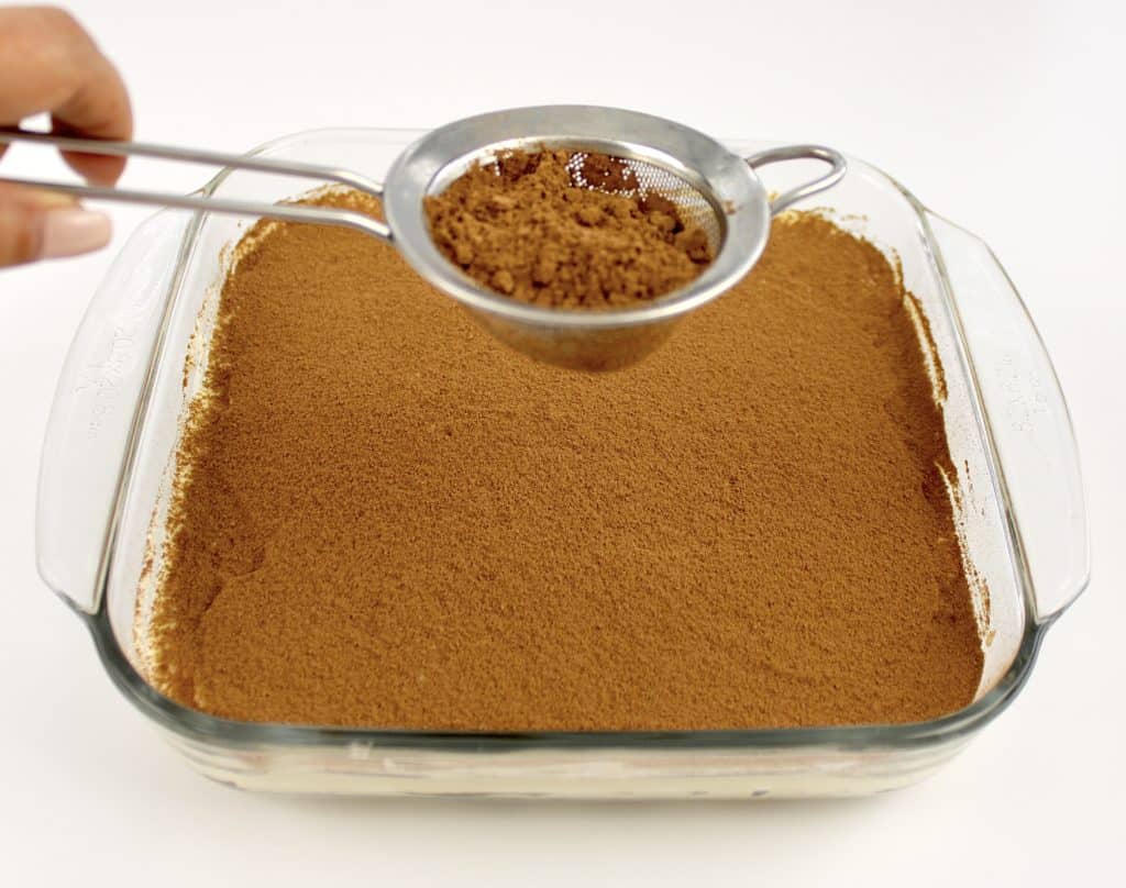 cocoa powder being sifted over glass baking dish