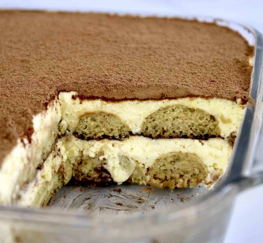 side view of tiramisu in glass dish with piece missing