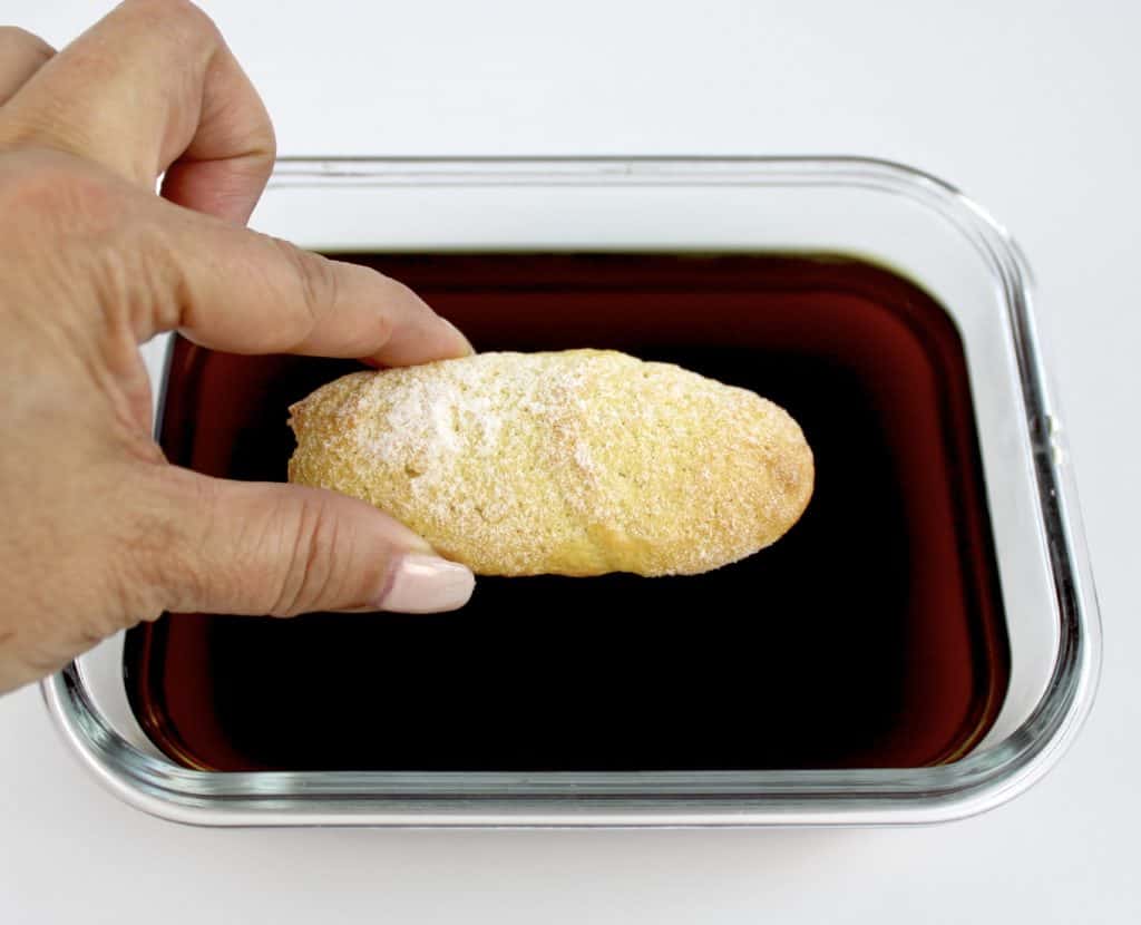 ladyfinger being dipped into coffee in square glass dish