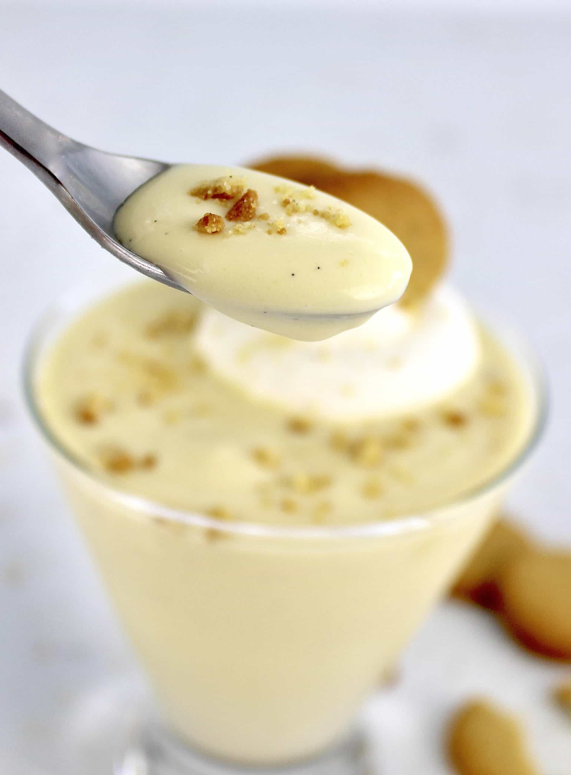 vanilla pudding in glass with spoon holding up some