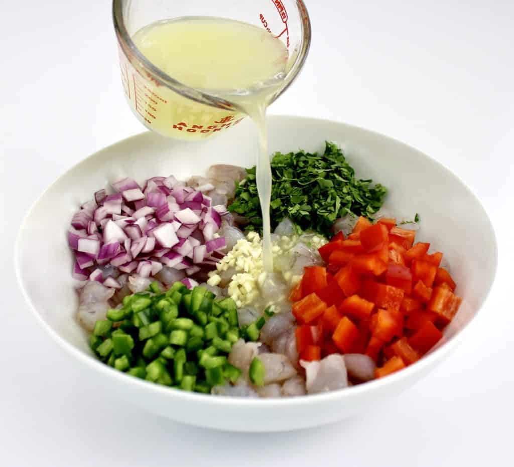 lime juice being poured over white bowl with chopped peppers onions and garlic