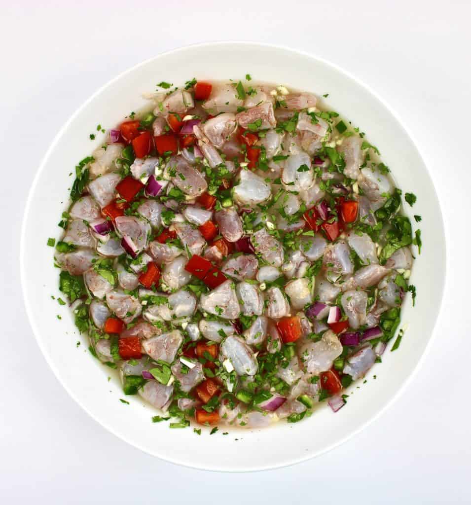 raw chopped shrimp peppers red onion and herbs in white bowl with lemon juice
