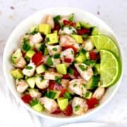 Shrimp Ceviche in white bowl with chopped veggies 2 lime slices