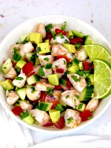Shrimp Ceviche in white bowl with chopped veggies 2 lime slices