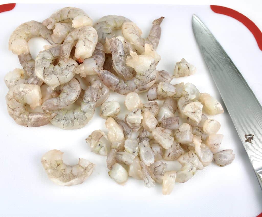 raw shrimp being chopped on white cutting board with knife on side
