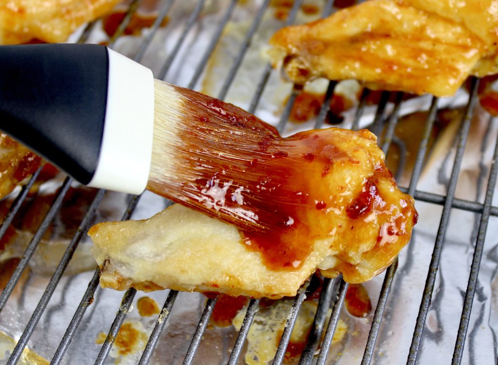 chicken wing on baking rack being brushed with asian wing sauce