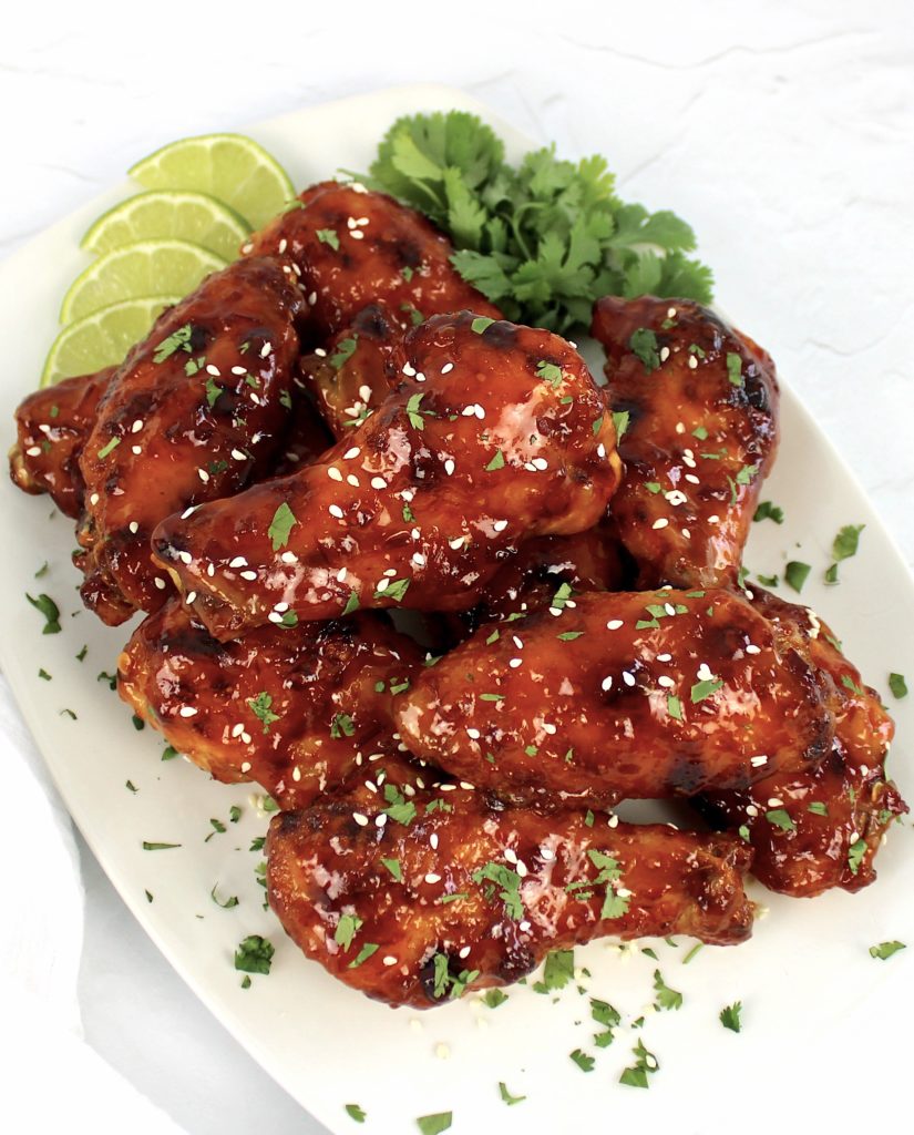 Sticky Asian Chicken Wings piled up on white plate with lime slices and cilantro