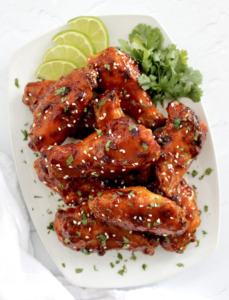 overhead view of Sticky Asian Chicken Wings on white plate with lime slices and cilantro garnish