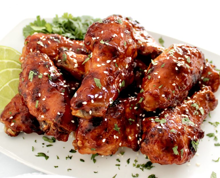closeup of Sticky Asian Chicken Wings piled up on white plate with cilantro garnish