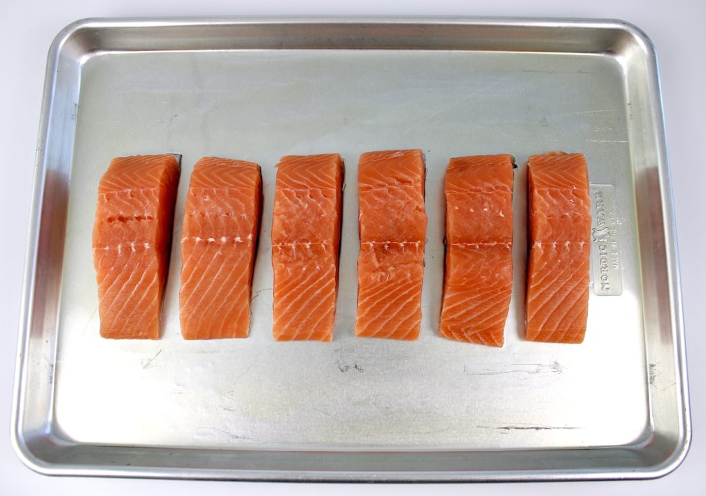 6 pieces of raw salmon lined on up baking sheet