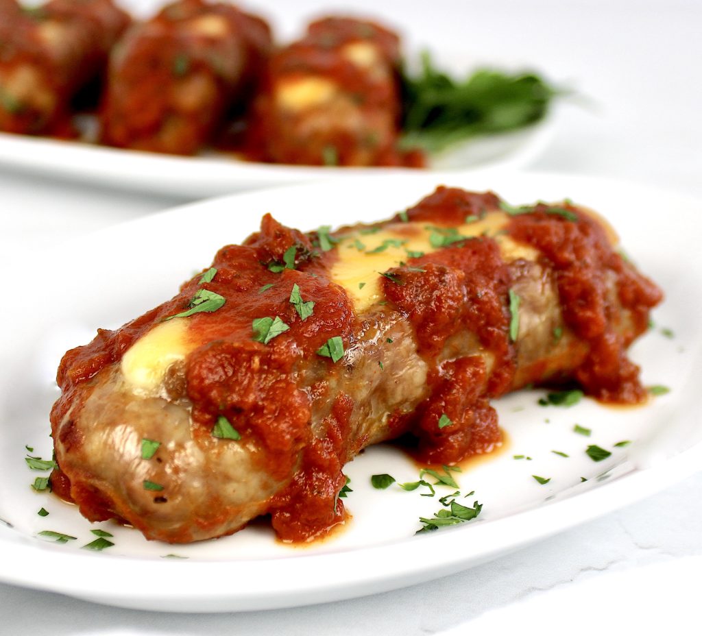 closeup of cheese stuffed sausage on white plate with marinara sauce on top
