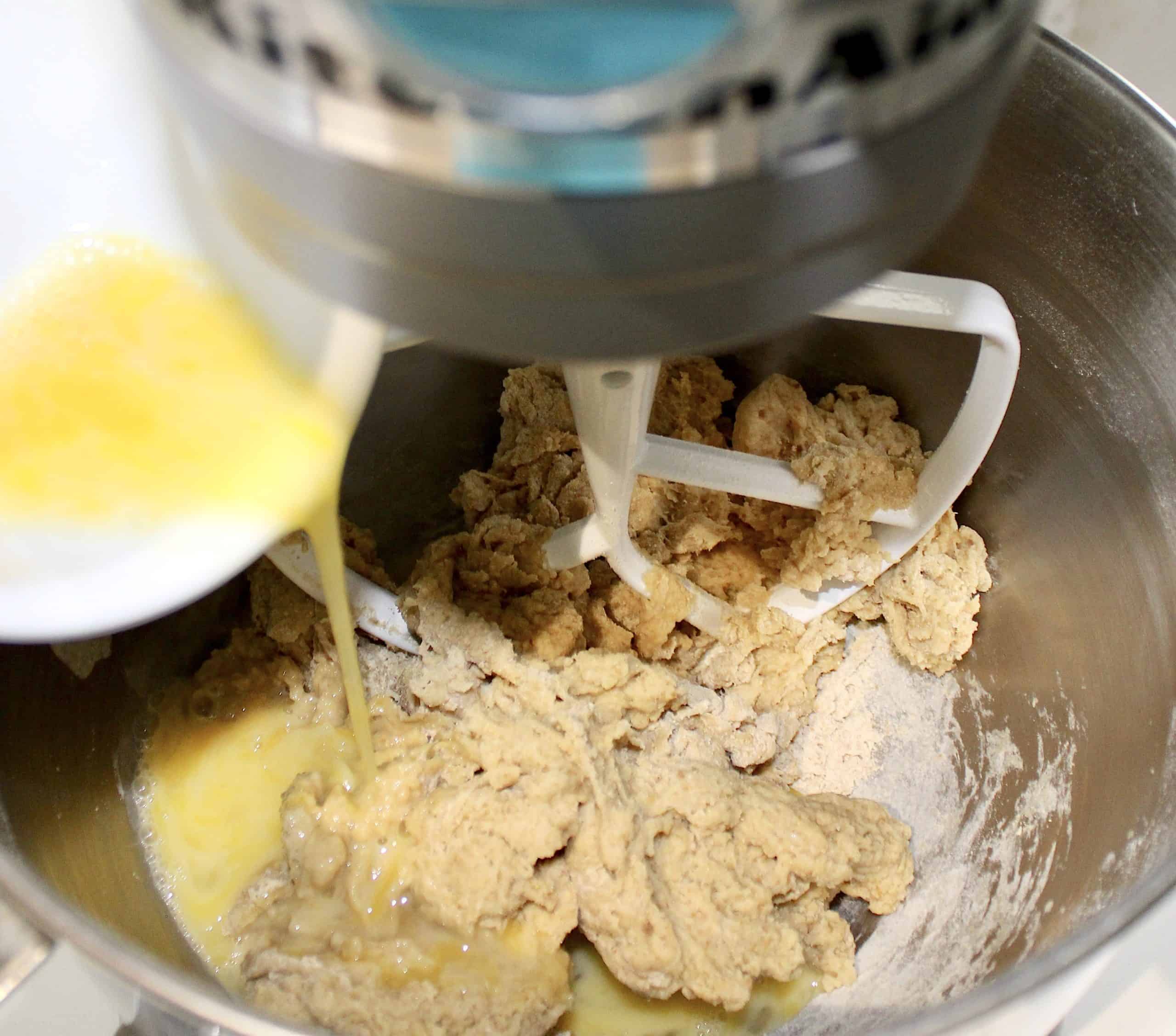 beaten eggs pouring into stand mixer with dough