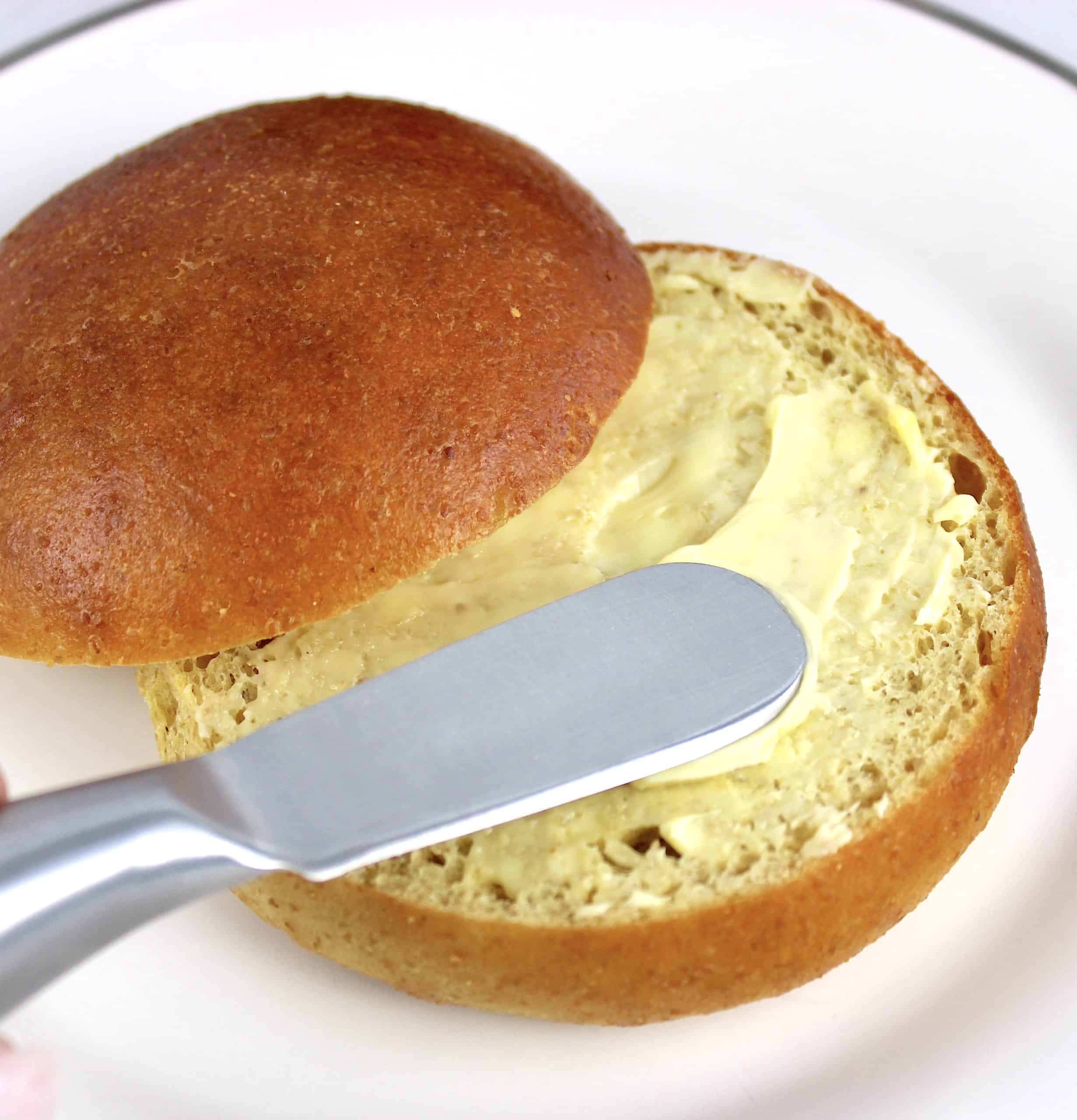keto bun sliced open with butter being spread on