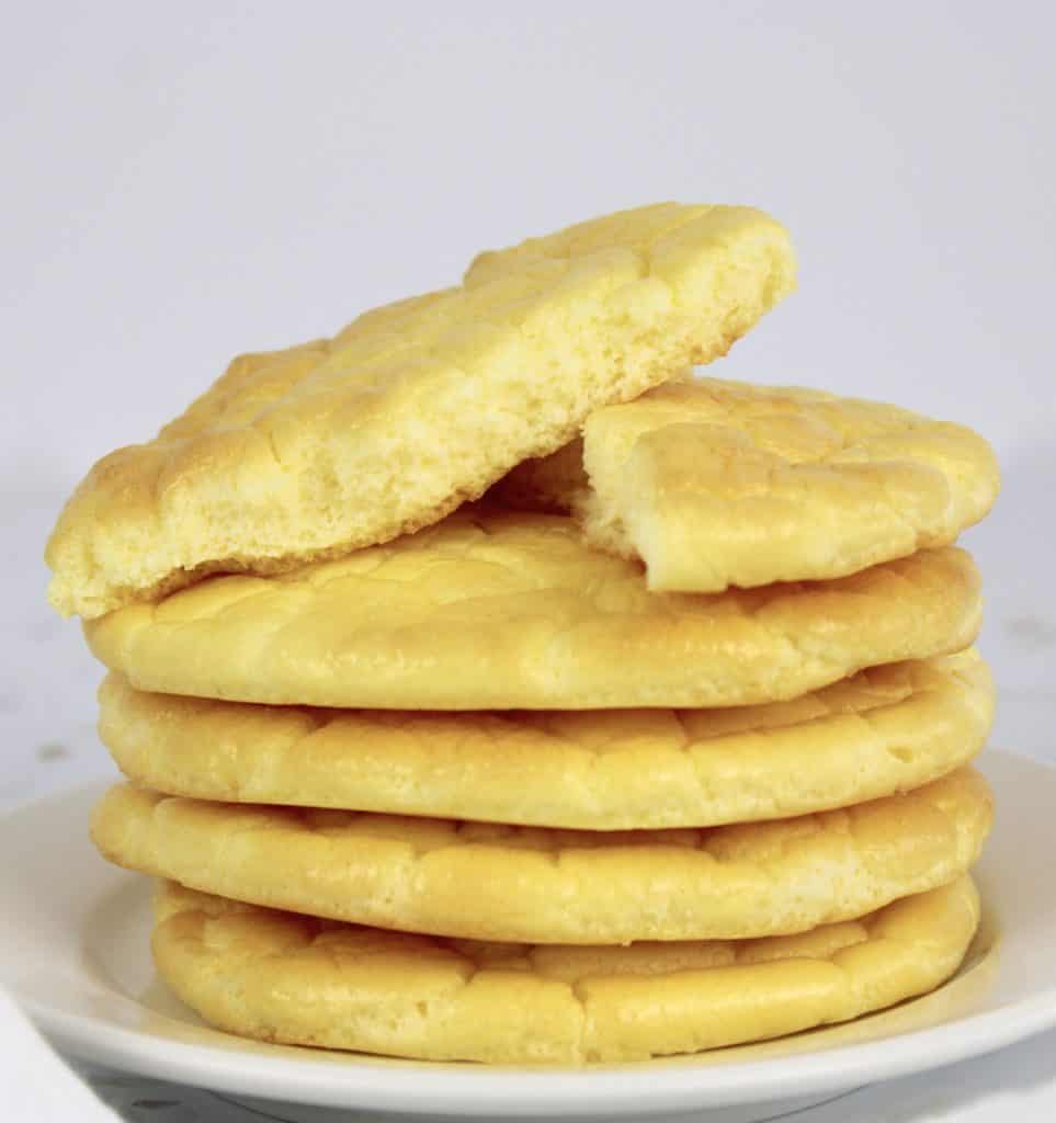 4 pieces cloud bread stacked on white plate with one piece cut on half on top