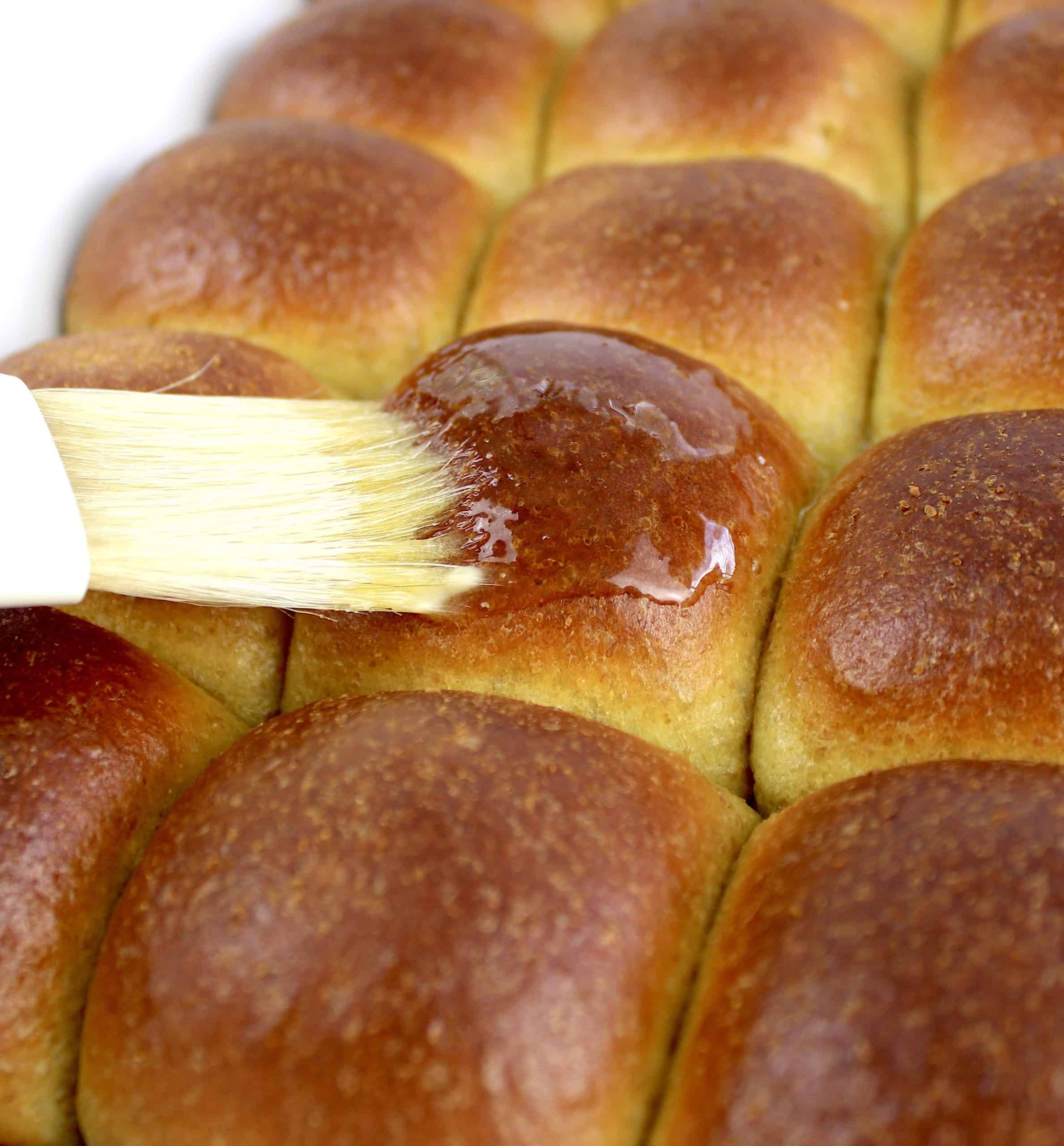 closeup of baked dinner rolls being brushed with melted butter
