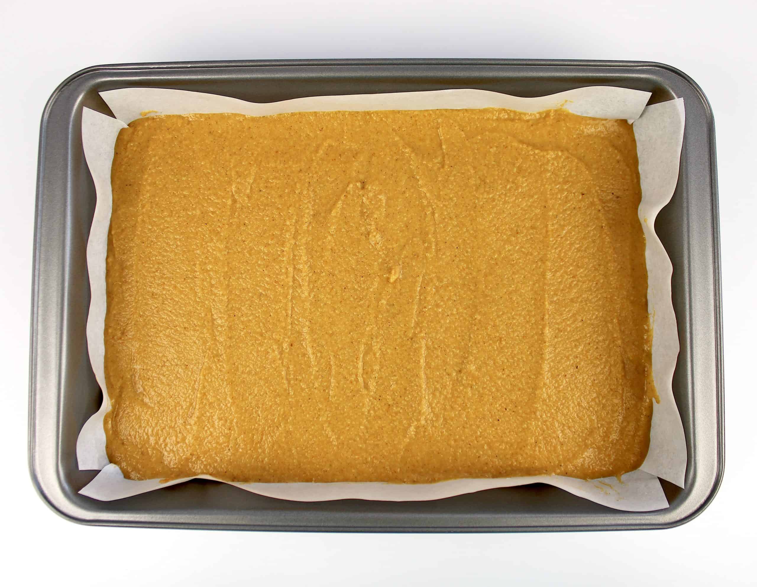 pumpkin bars batter in baking pan with parchment paper unbaked