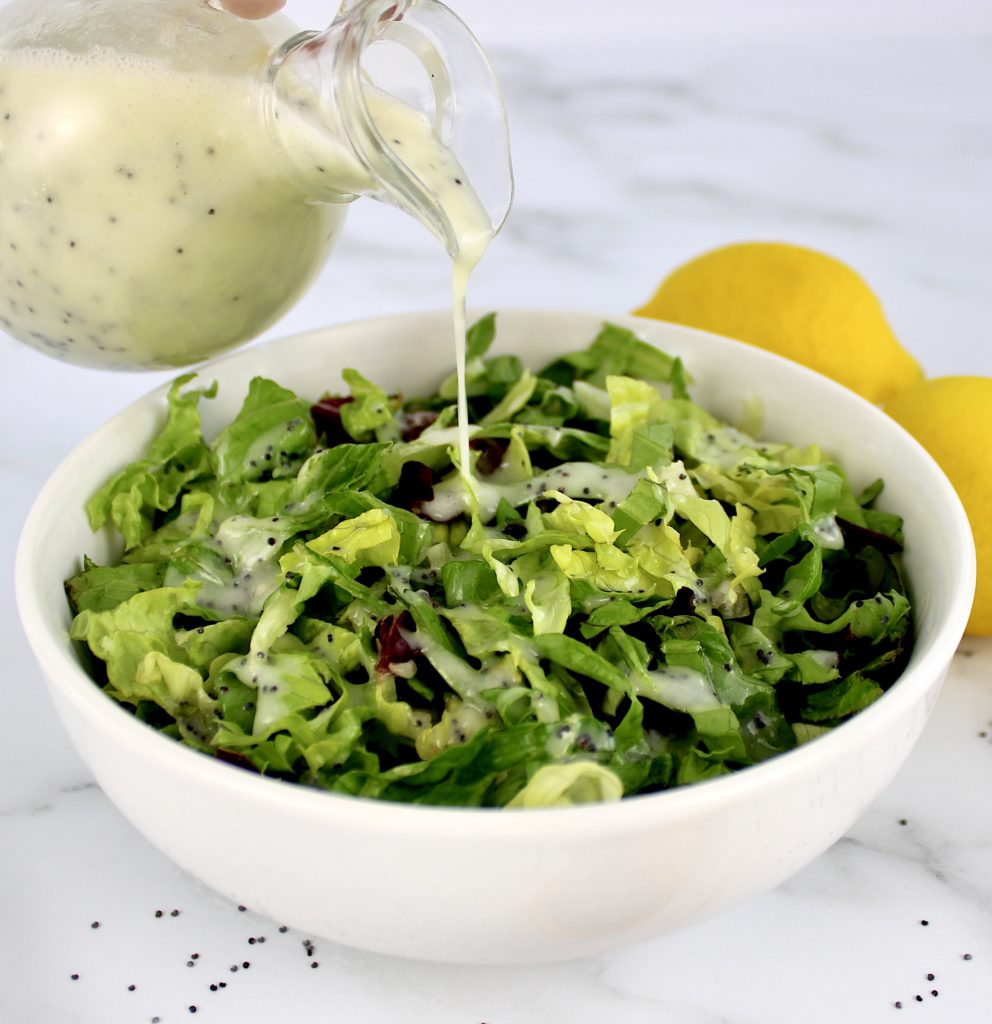 Lemon Poppy Seed Dressing in glass bottle being poured over salad in white bowl