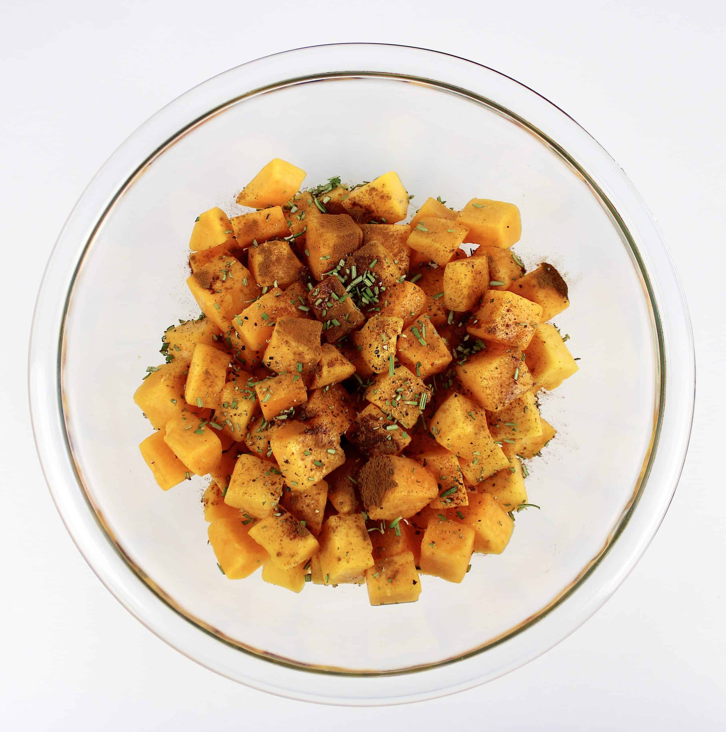 cubed butternut squash in glass bowl with spices on top