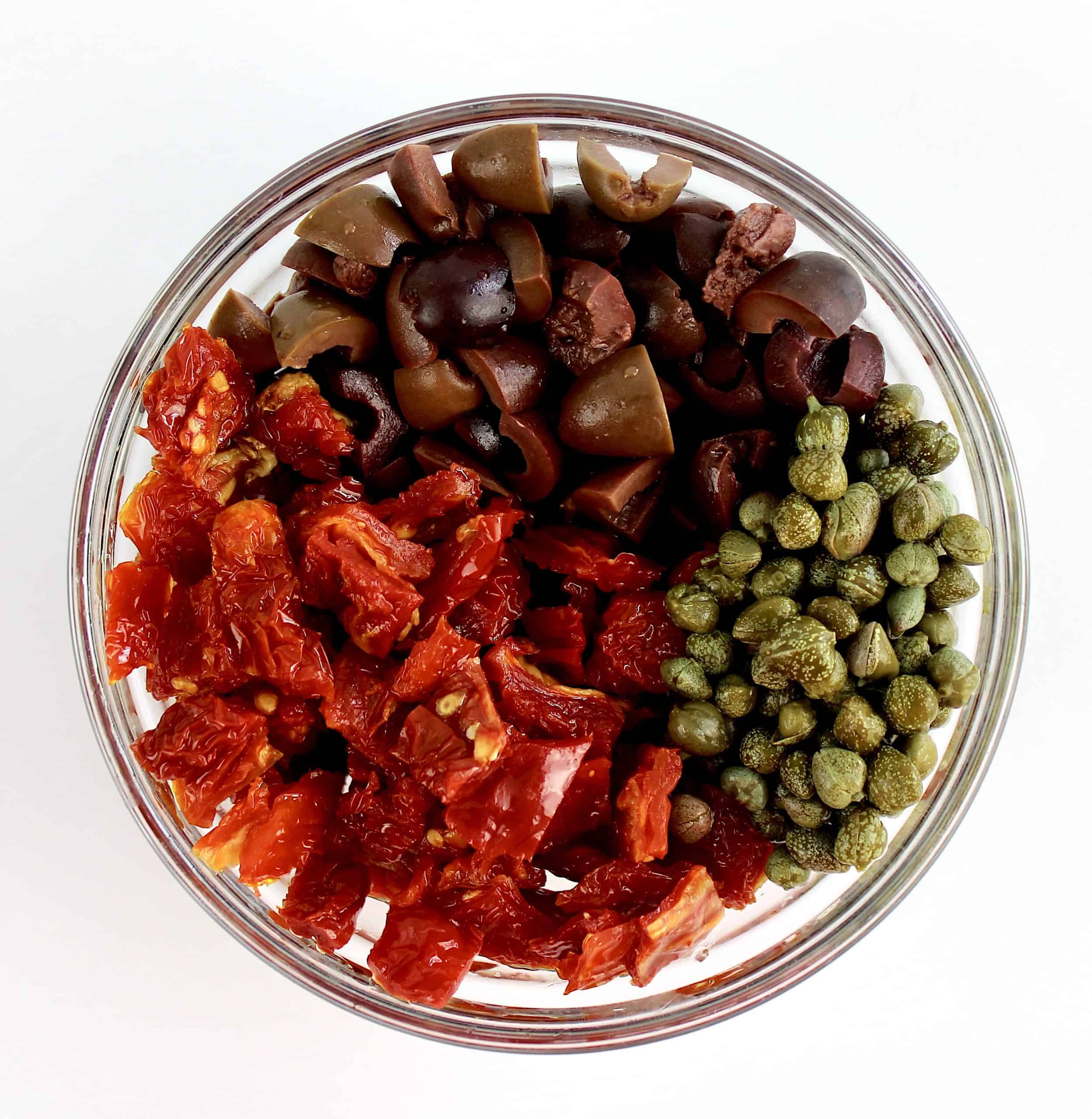 chopped olives sun-dried tomatoes and capers in glass bowl