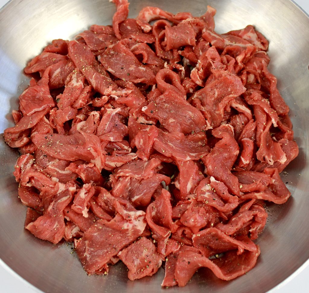 thinly sliced steak in skillet with salt and pepper