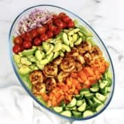 salad with rows of shrimp avocado tomatoes peppers onions in glass bowl
