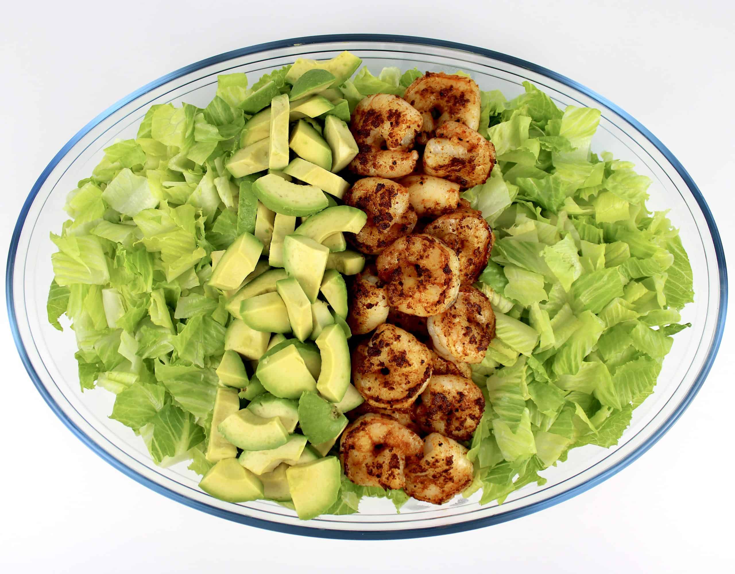 glass bowl with chopped lettuce shrimp and sliced avodao