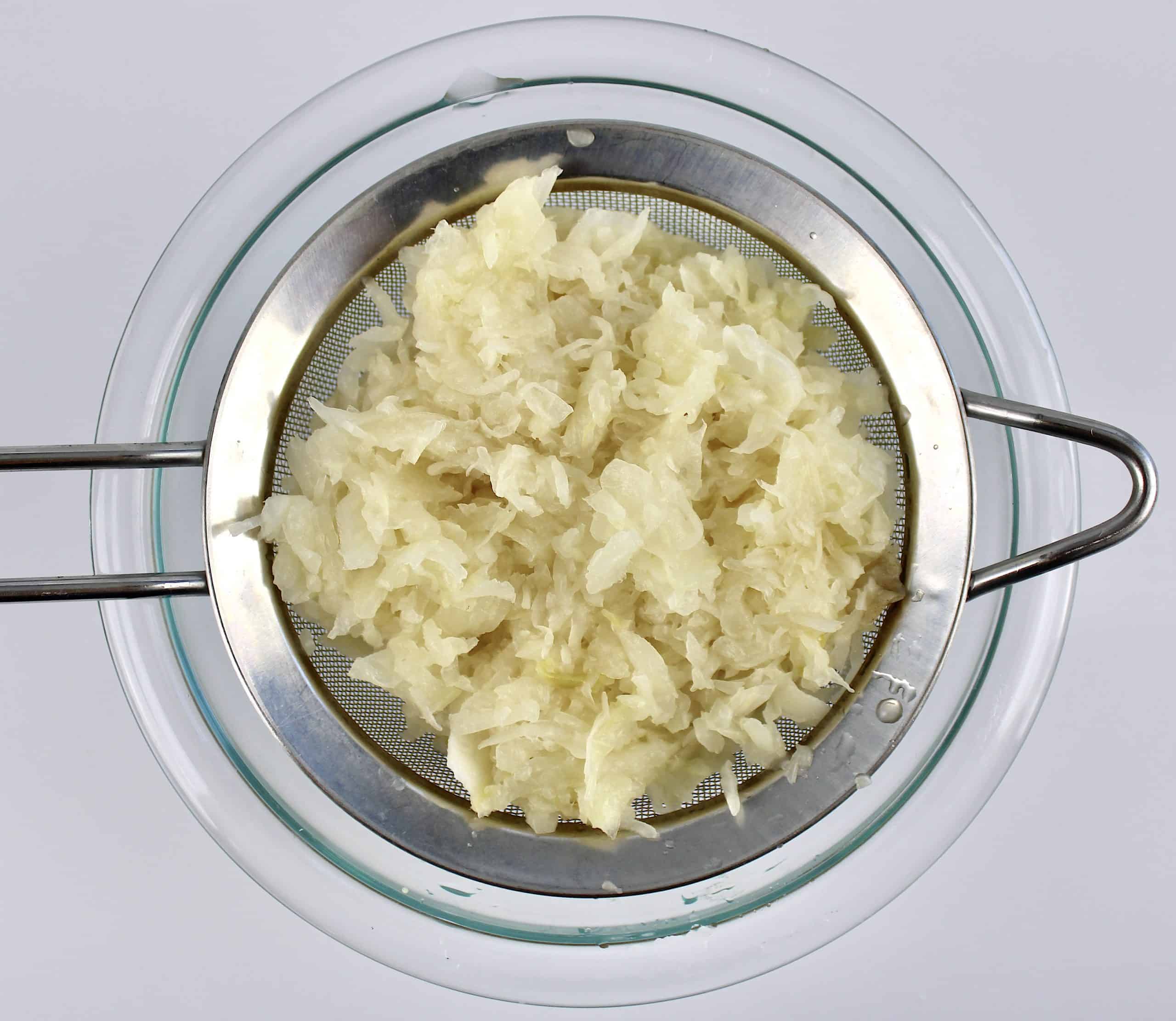 Sauerkraut in metal strainer over glass bowl