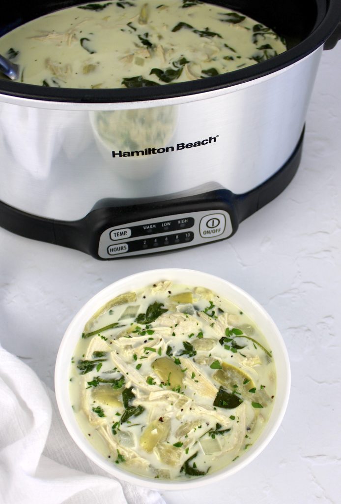 Spinach Artichoke Chicken Soup in white bowl with slow cooker in background