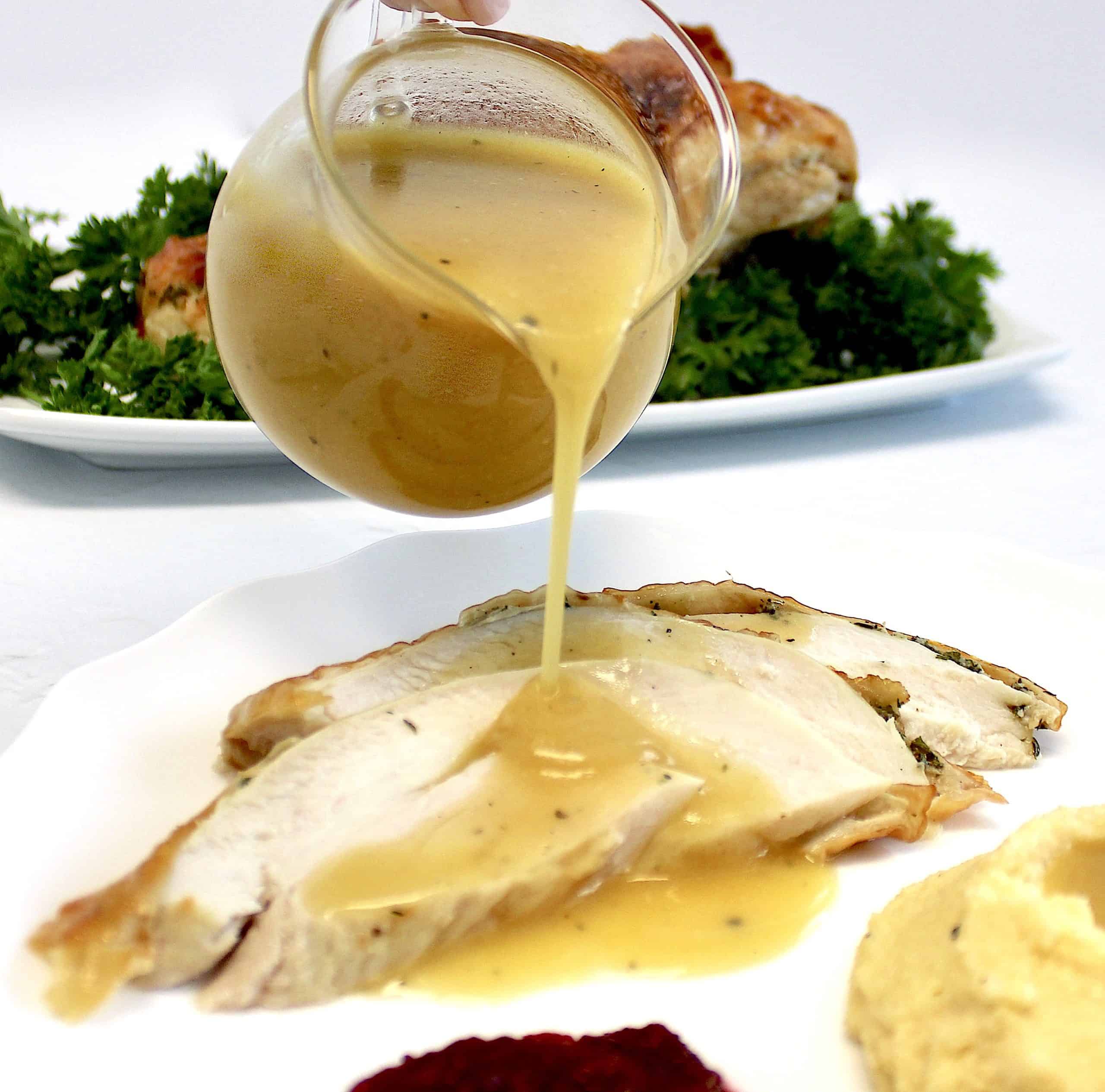 gravy being poured over slices of turkey on white plate