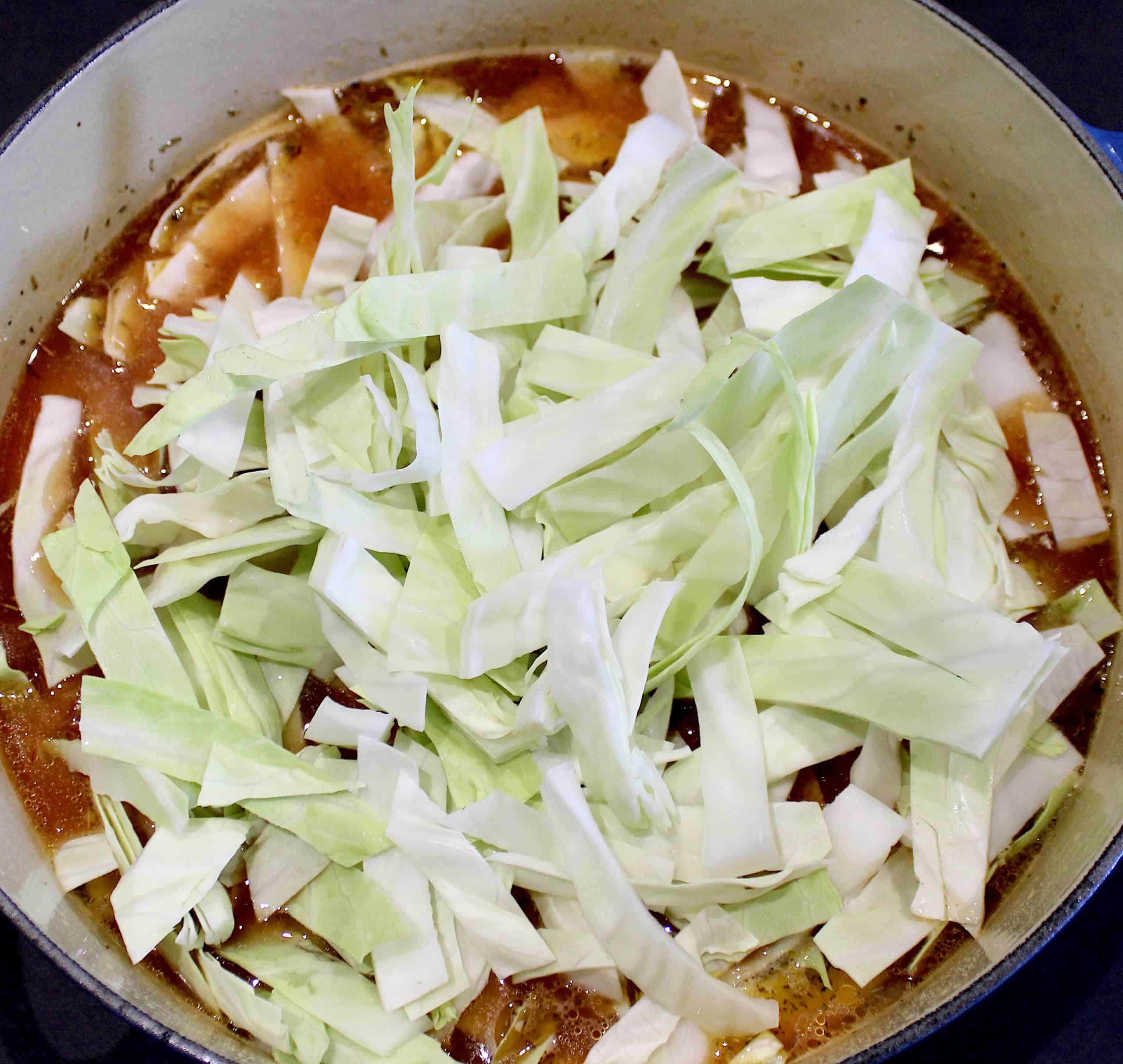 shredded cabbage over soup in pot