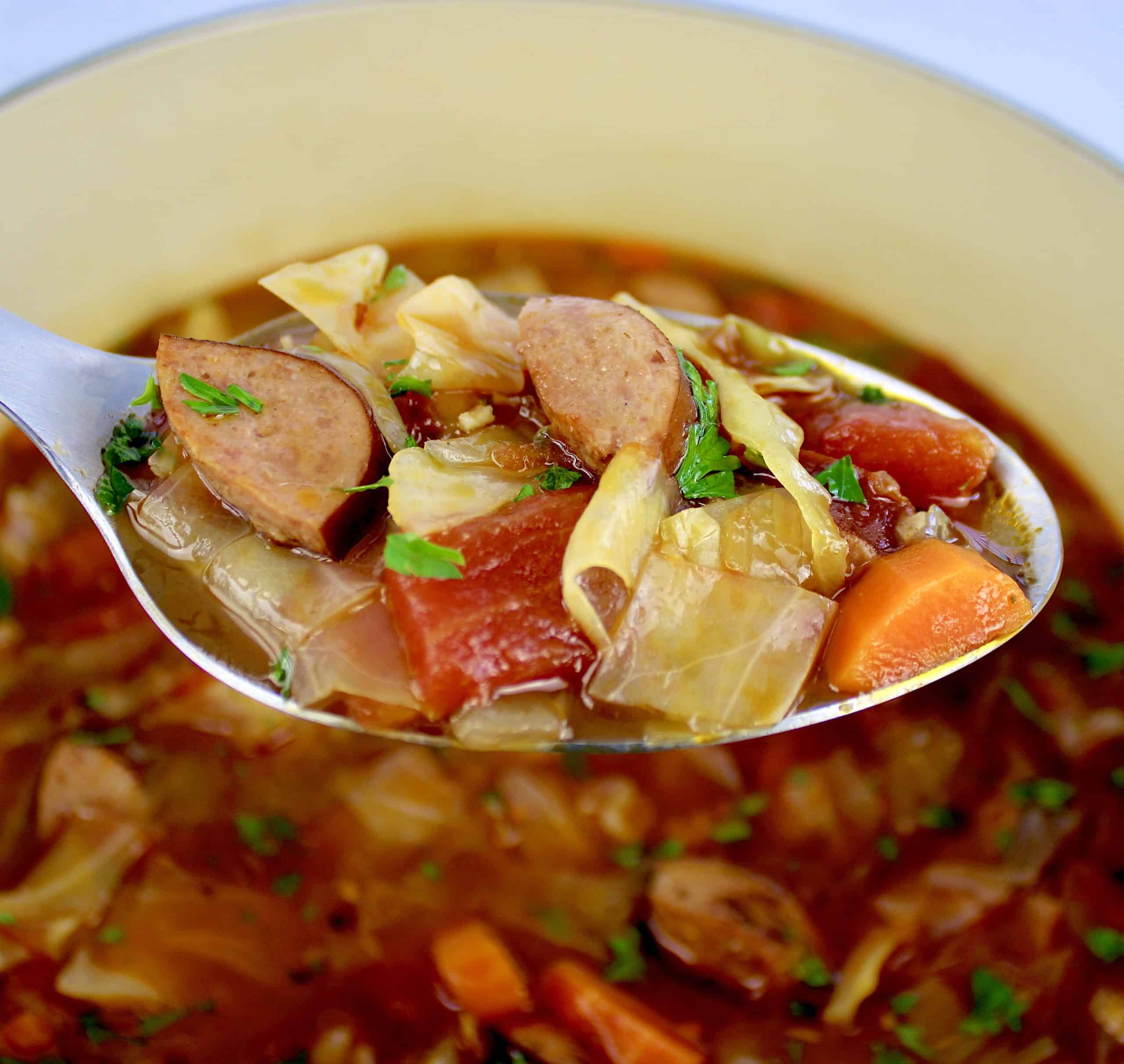 ladle full of cabbage soup with sausage held over pot