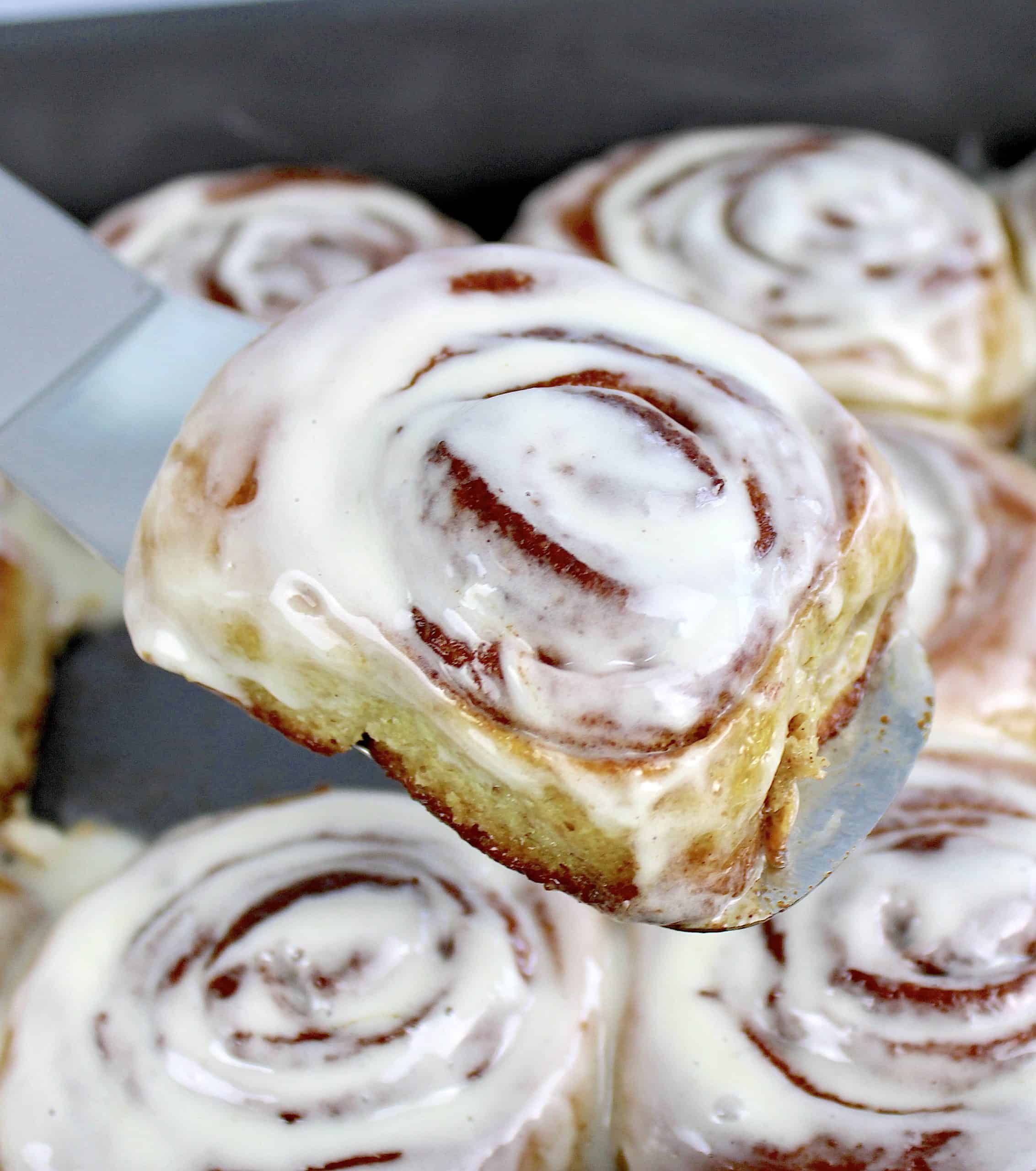 iced cinnamon roll held up by spatula