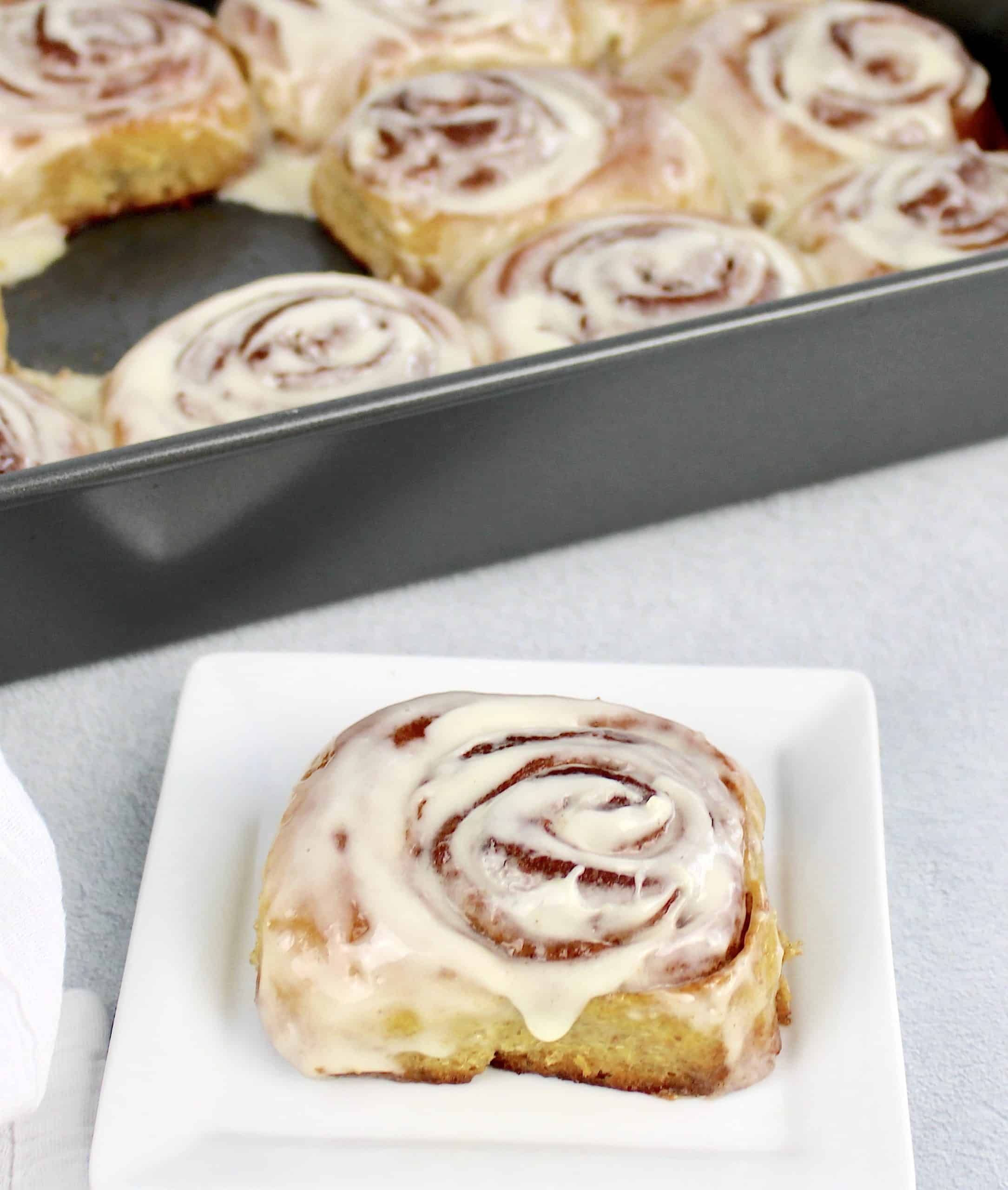 cinnamon roll with icing on white plate with baking pan in background
