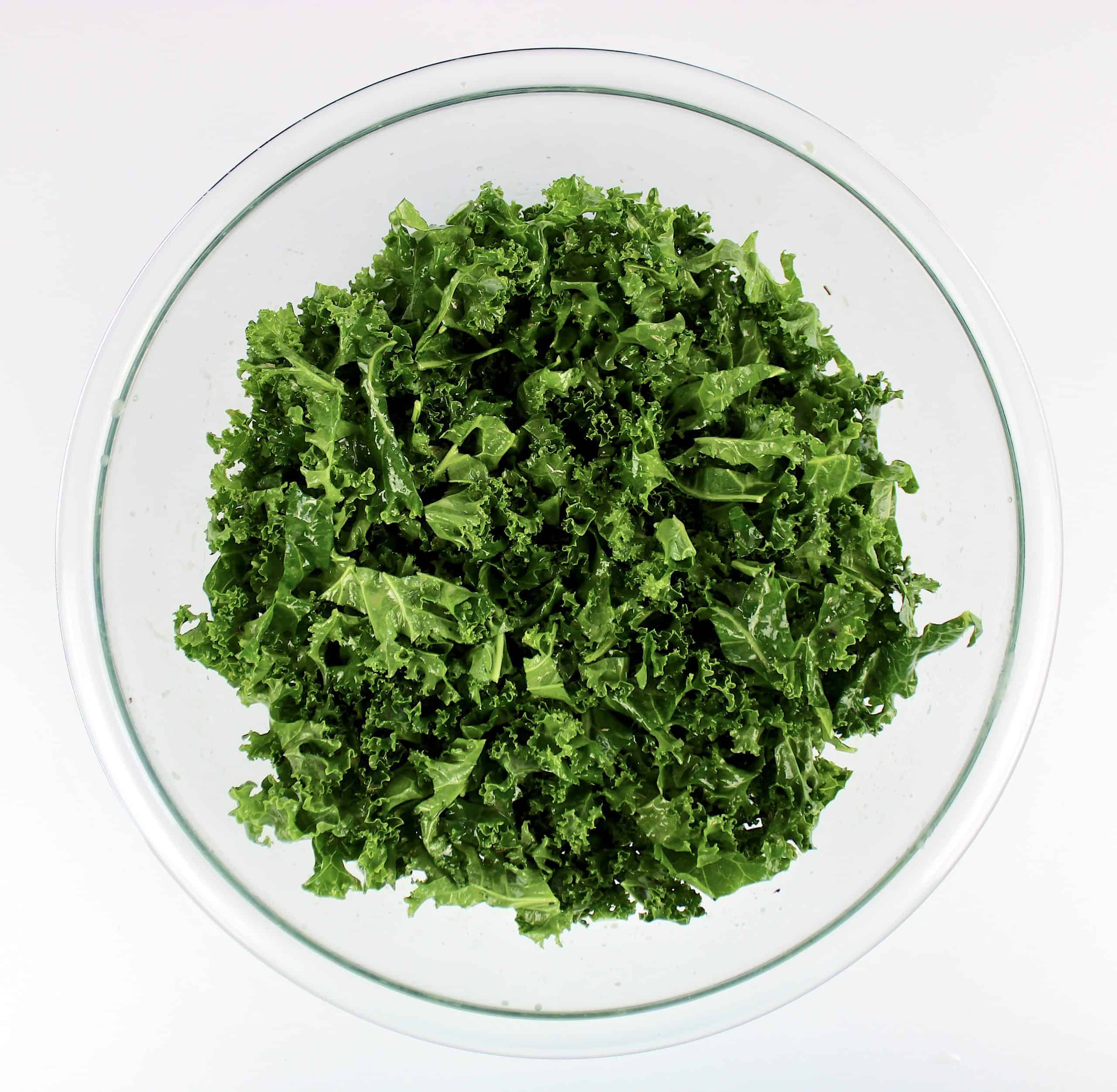 chopped kale in glass bowl with dressing mixed in