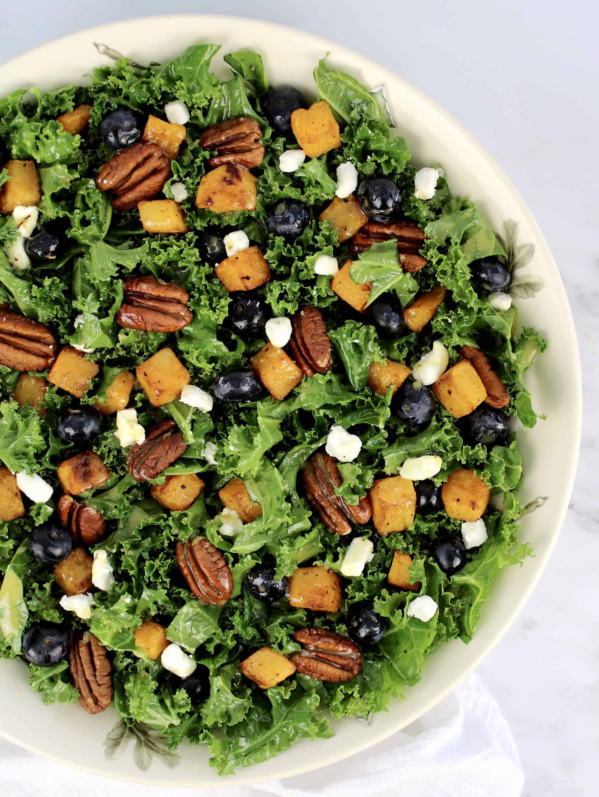 kale salad with butternut squash pecans blueberries in bowl in white bowl