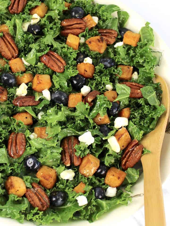 kale salad with butternut squash pecans blueberries in bowl with wooden spoon