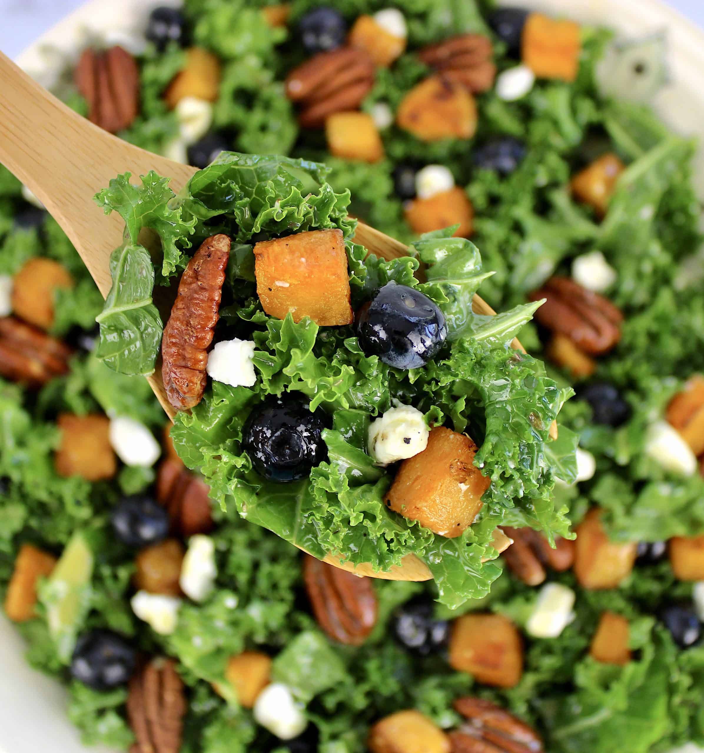 kale salad with butternut squash blueberries and pecan in wooden spoon